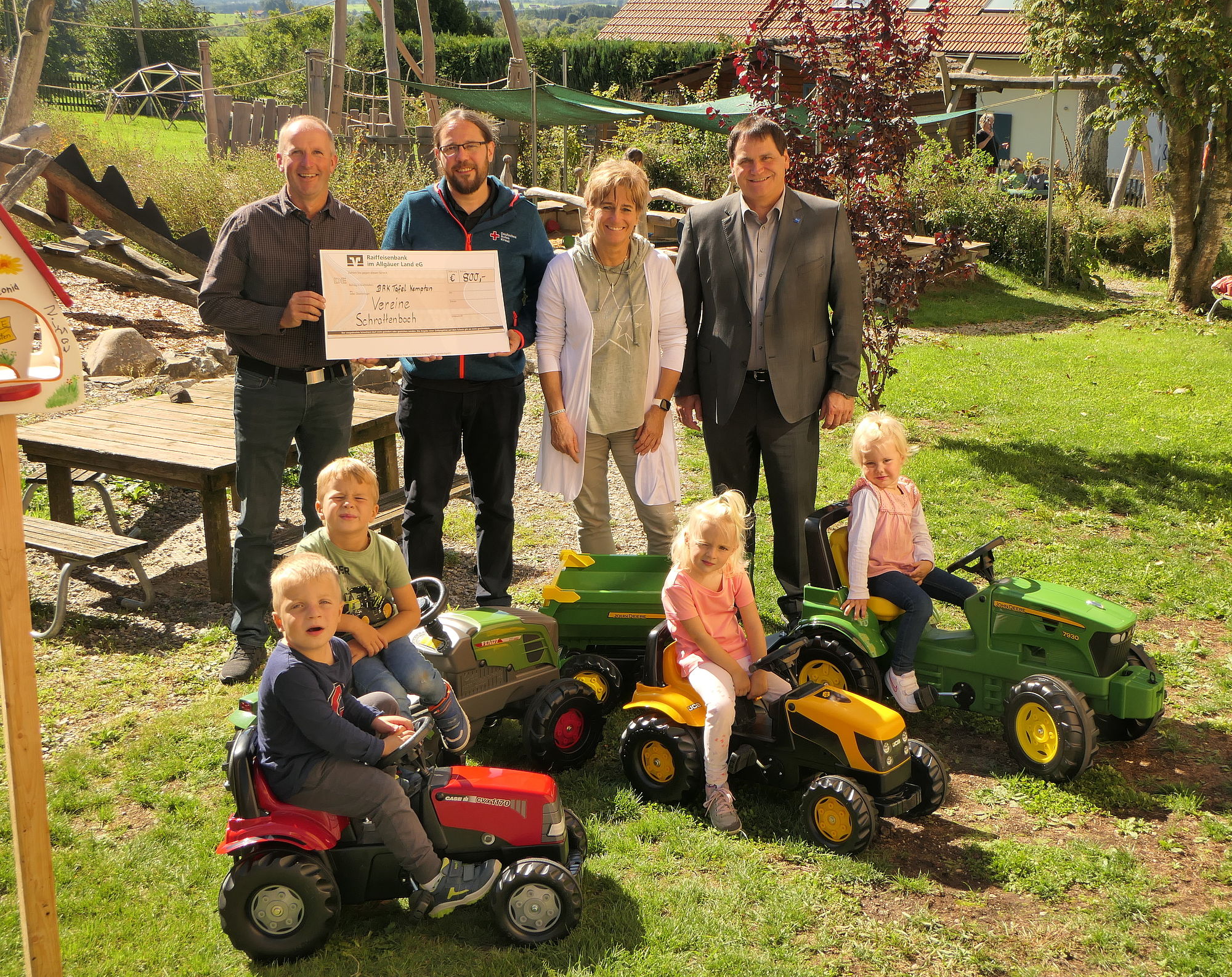 Auf dem Bild sind 4 Erwachsene und 4 Kinder zu sehen. Zwei erwachsene Männer halten einen Spendenscheck in der Hand.